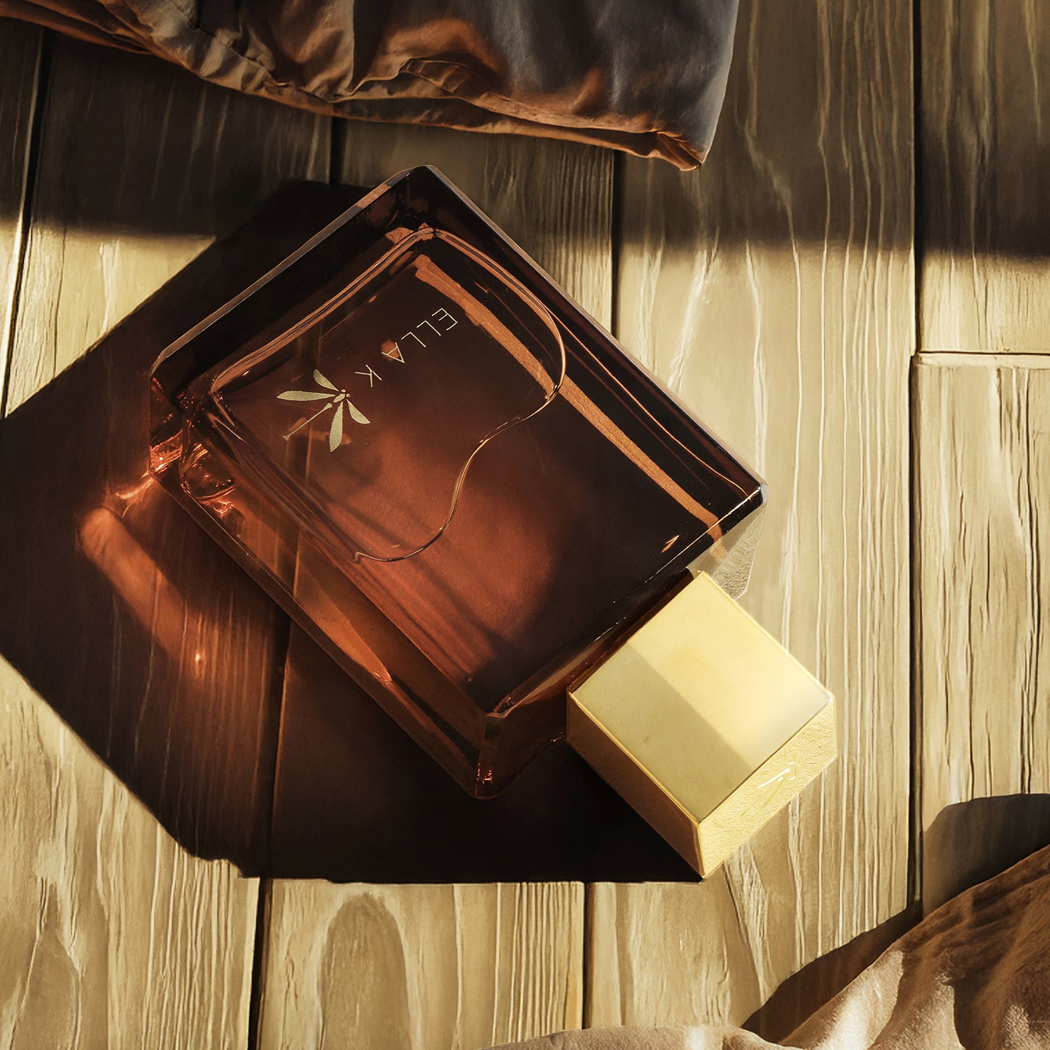 Flacon du parfum Amber K d’Ella K posé sur du bois à la lumière du soleil