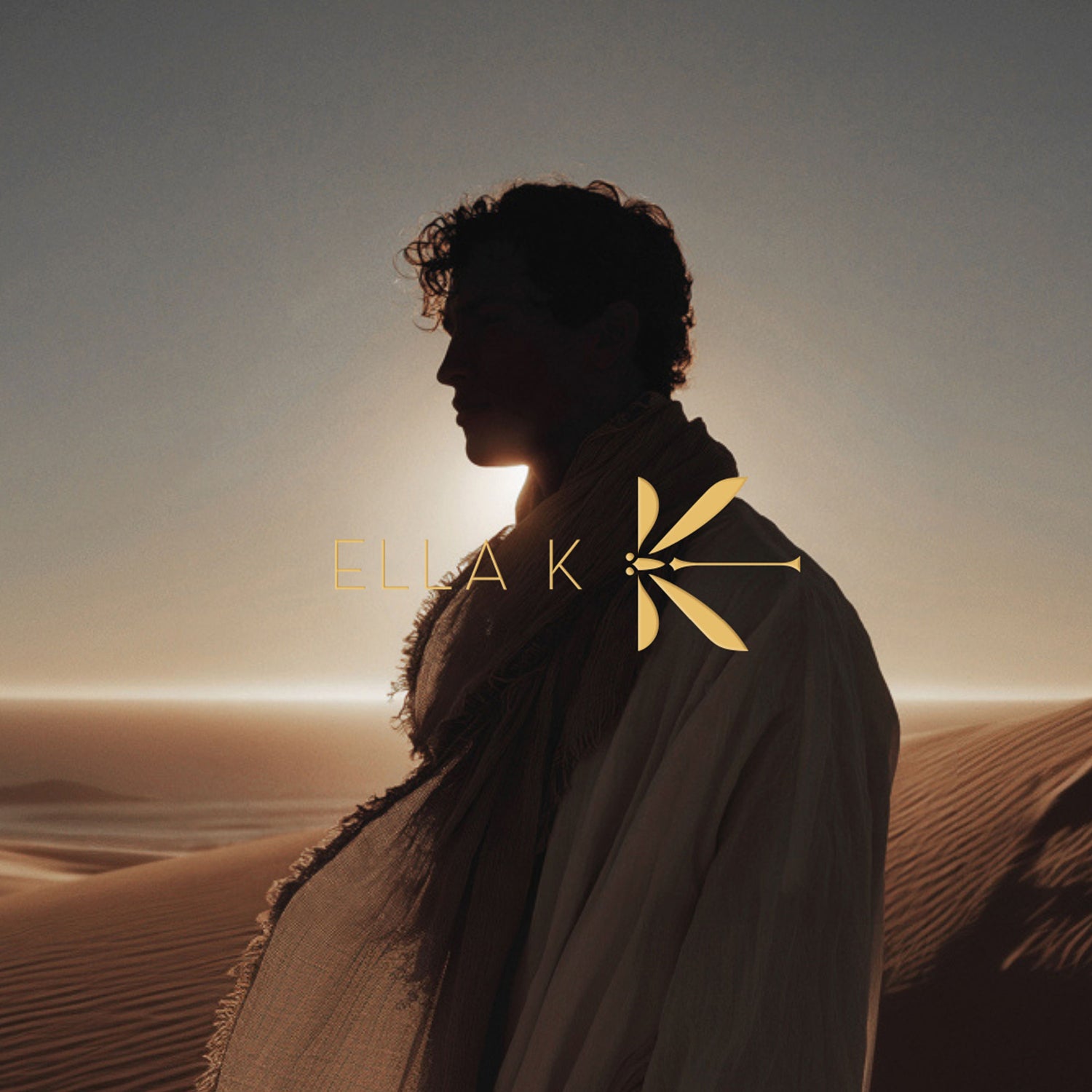 Silhouette d’un homme en profil, vêtu d’un châle et de vêtements traditionnels, devant un coucher de soleil dans les dunes. Le logo Ella K est superposé.