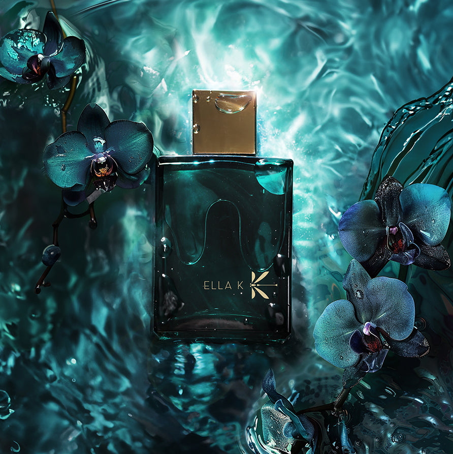 Le flacon d’Orchid K d’Ella K Parfums flotte dans un tourbillon d’eau, entouré d’orchidées bleu nuit – une signature olfactive puissante et mystérieuse.