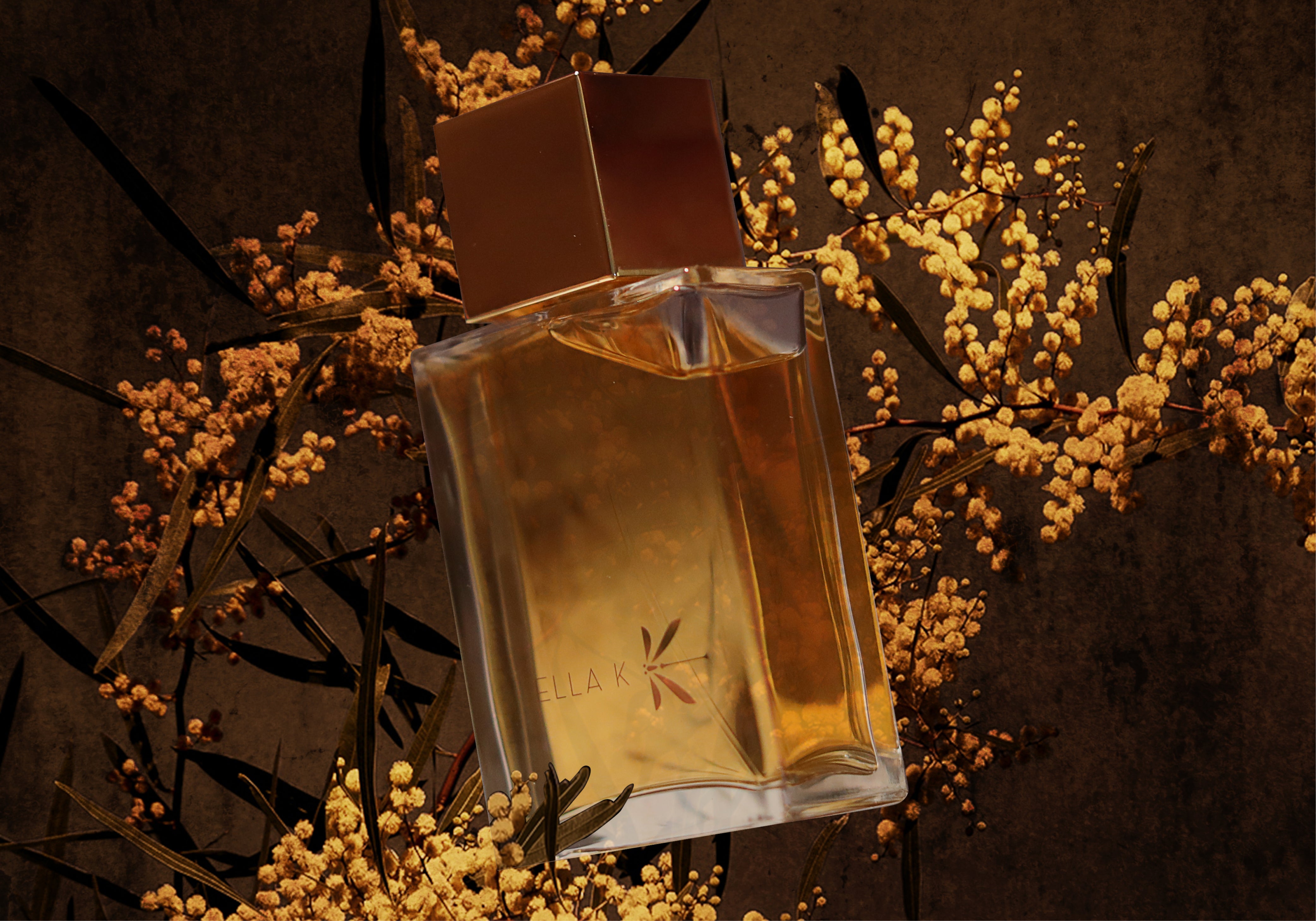 Flacon Reflet de l’Okavango d’Ella K parmi fleurs de mimosa jaunes sur fond sombre – expression de sensualité botanique et inspiration africaine.