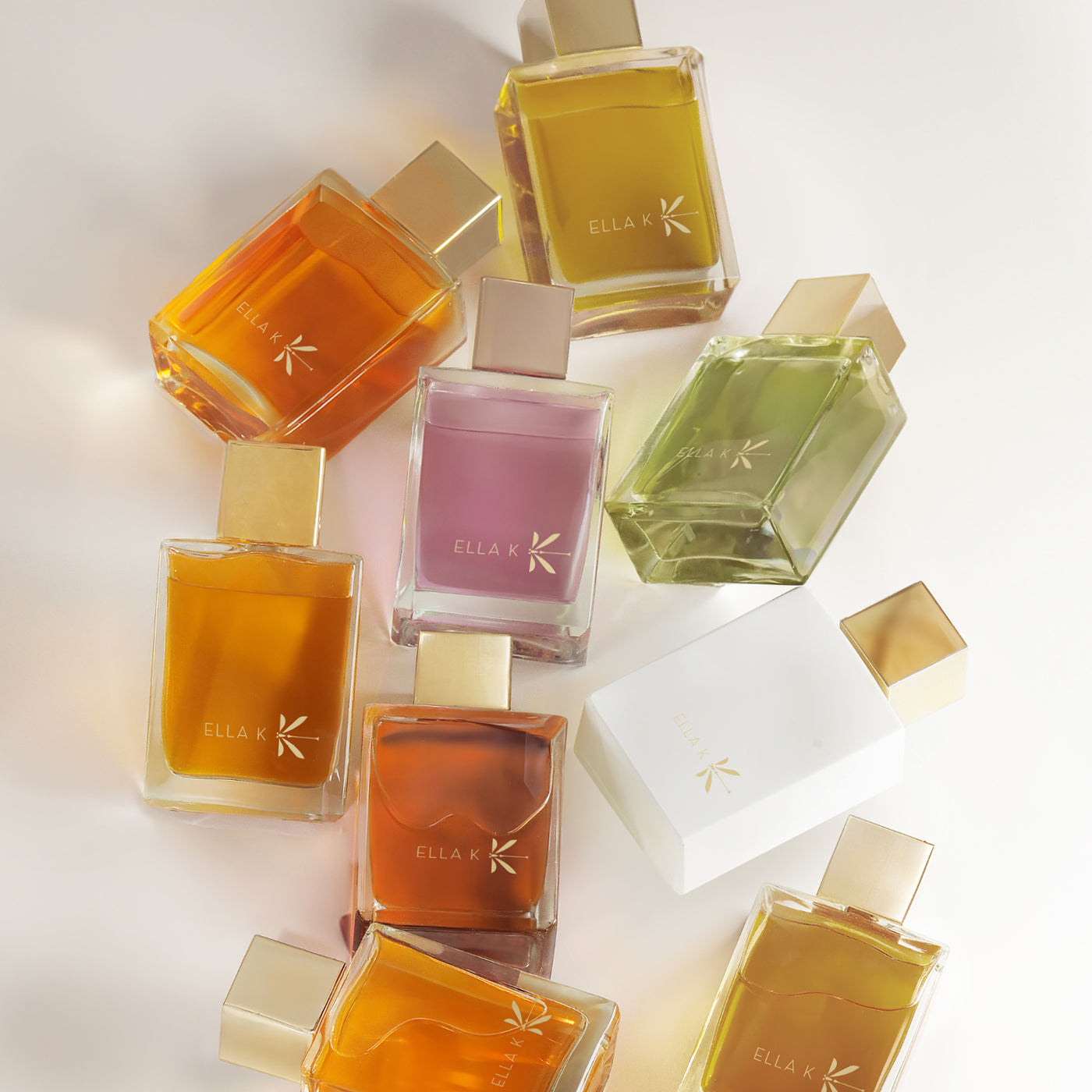 Composition of all Ella K bottles – eleven eaux de parfum in various colours with gold caps, arranged on a light background.