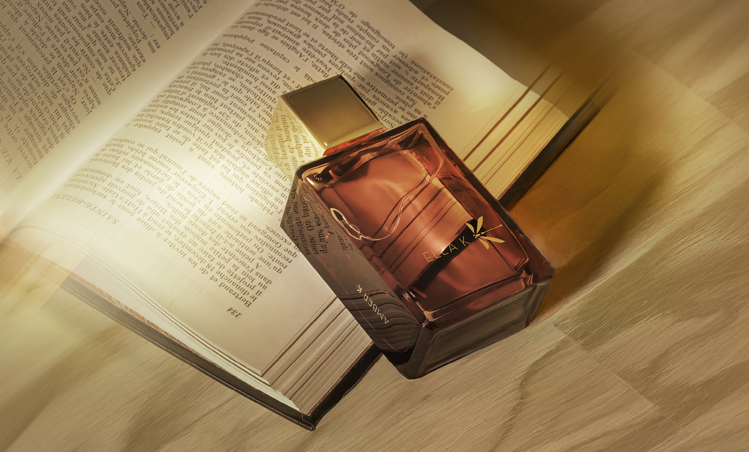 Amber K Eau de Parfum par Ella K – posé sur un livre ouvert, baigné de lumière dorée.