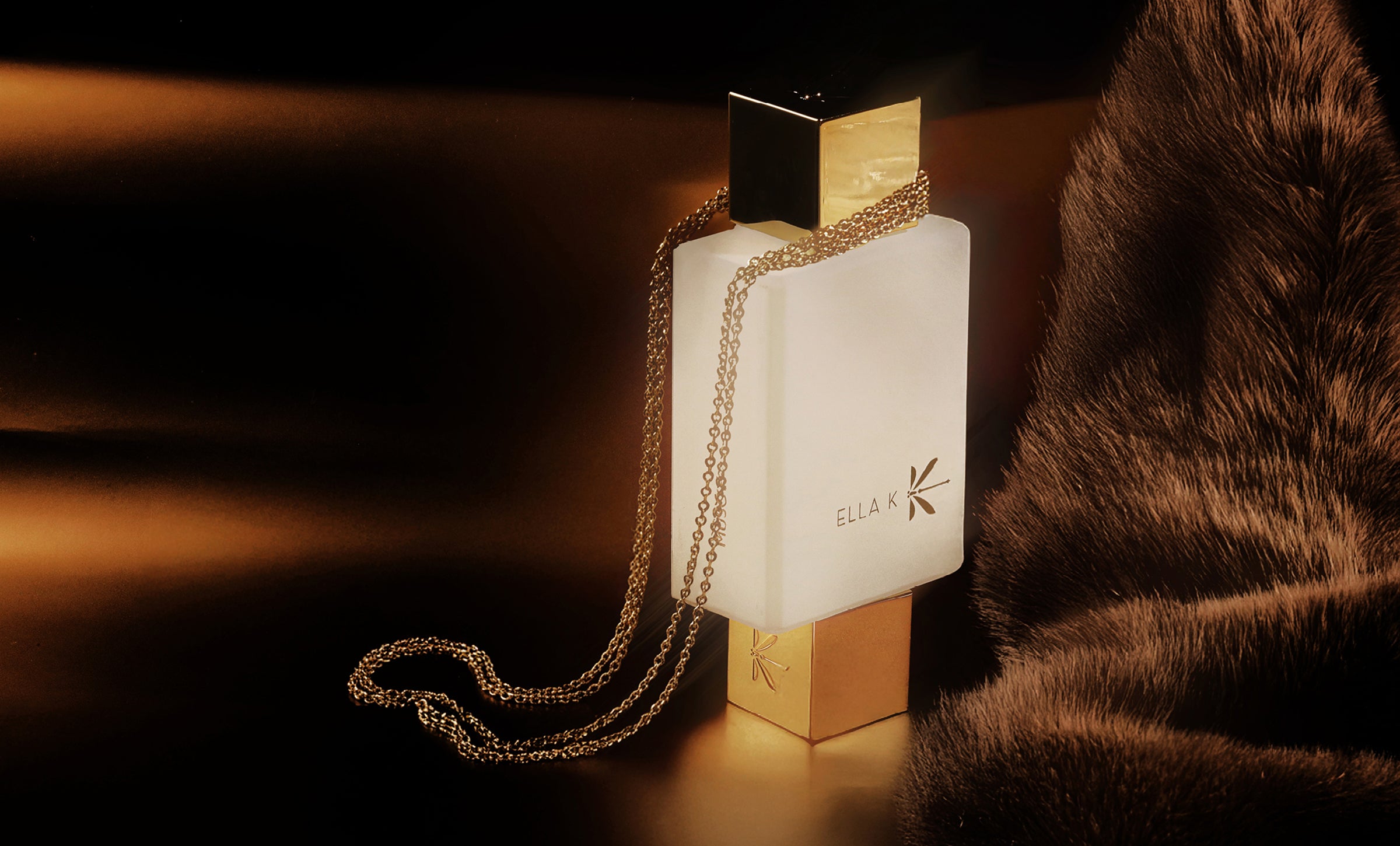 Flacon de « Musc K » – flacon blanc orné d’une chaîne dorée sur fond de fourrure sombre, symbole de chaleur, de sensualité et d’élégance intemporelle d’Ella K Parfums.
