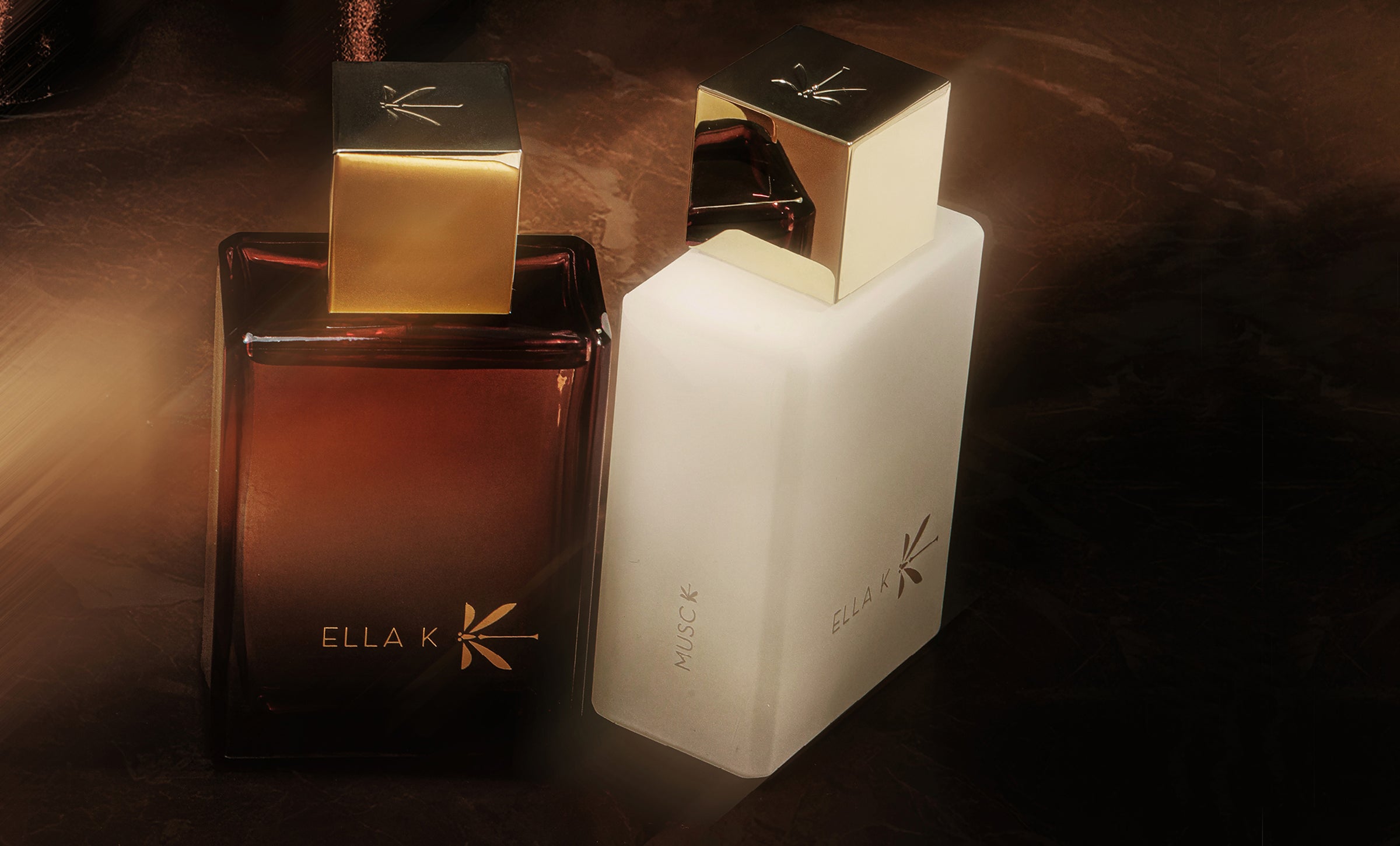 Flacons des parfums Ella K en blanc et ambre – « Musc K » et « Amber K » côte à côte sous une lumière chaude, symbole de la dualité et de l’harmonie de la collection.
