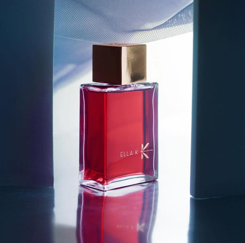 Flacon de parfum Ella K en rouge rubis lumineux – une mise en scène poétique entre ombre et lumière.