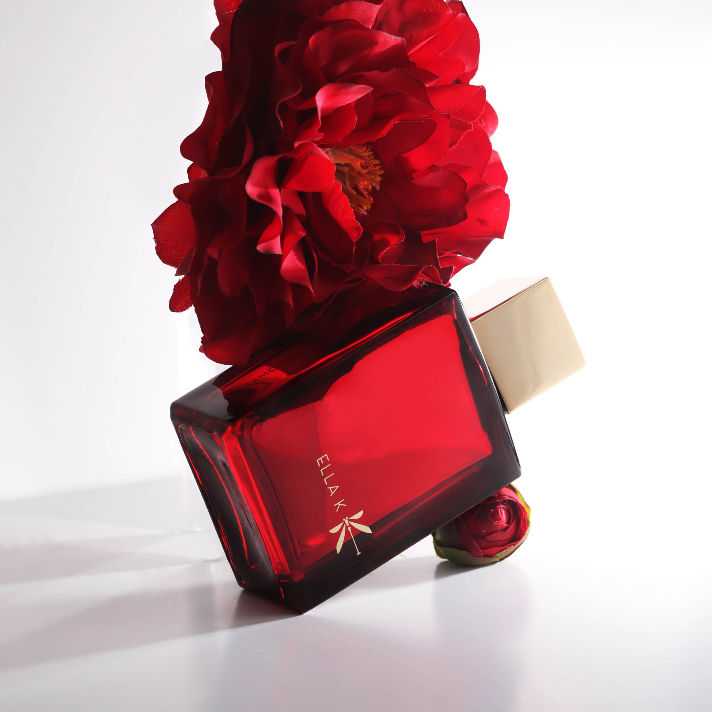 Flacon de parfum Camélia K en rouge profond, accompagné d’une fleur de camélia rouge luxuriante – symbole d’élégance sensuelle et d’intensité florale.