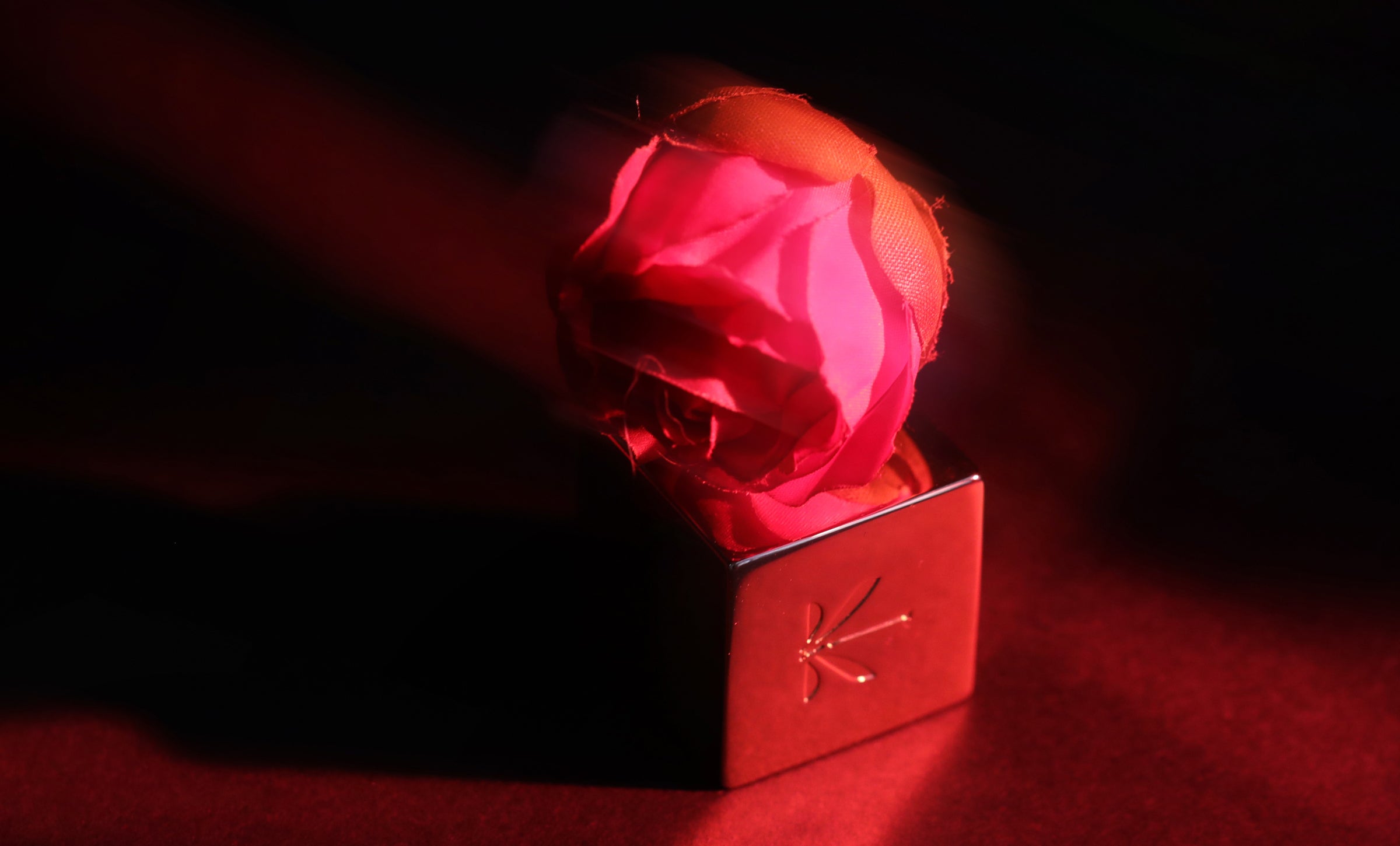 Détail artistique : une rose rose stylisée repose sur le bouchon gravé du parfum Camélia K d’Ella K.