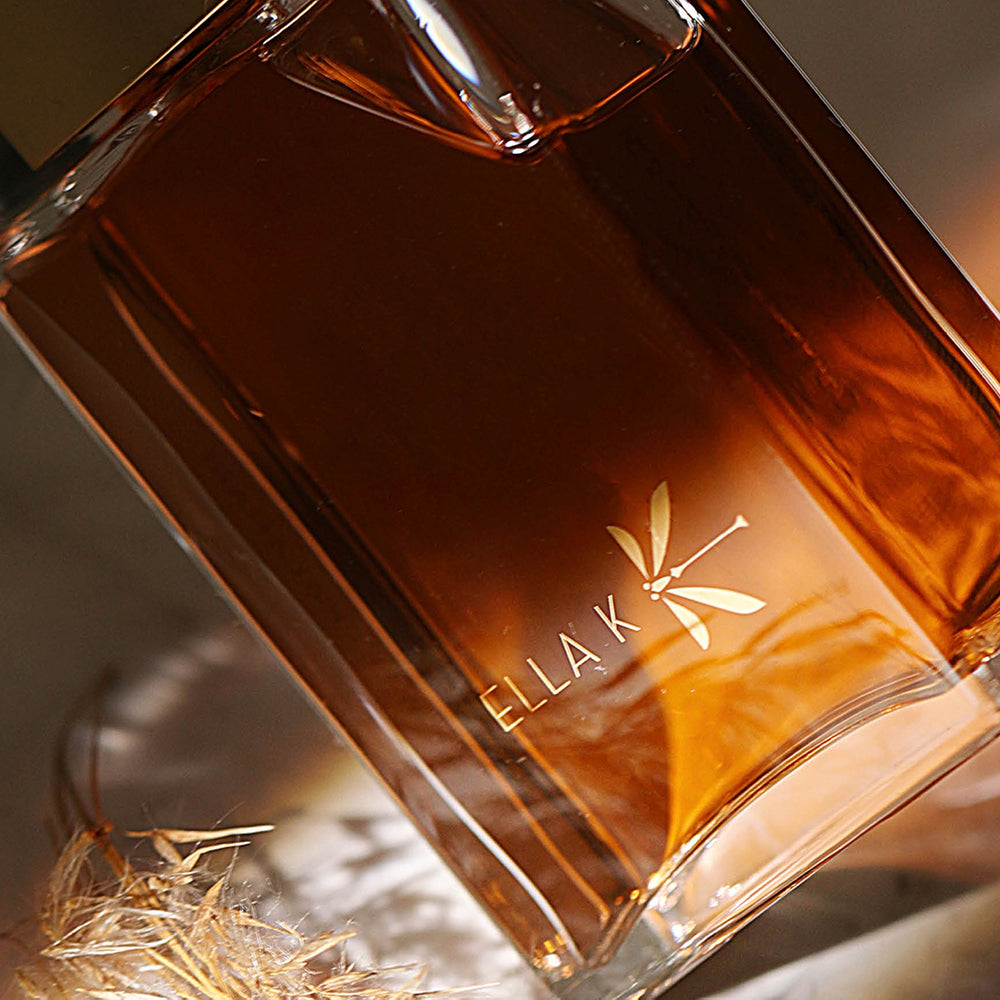 Flacon de Cri du Kalahari d’Ella K – jeu de lumière chaleureux sur le verre couleur ambre, entouré d’herbes sèches – évocation d’une chaleur sensuelle et de l’élégance du désert.