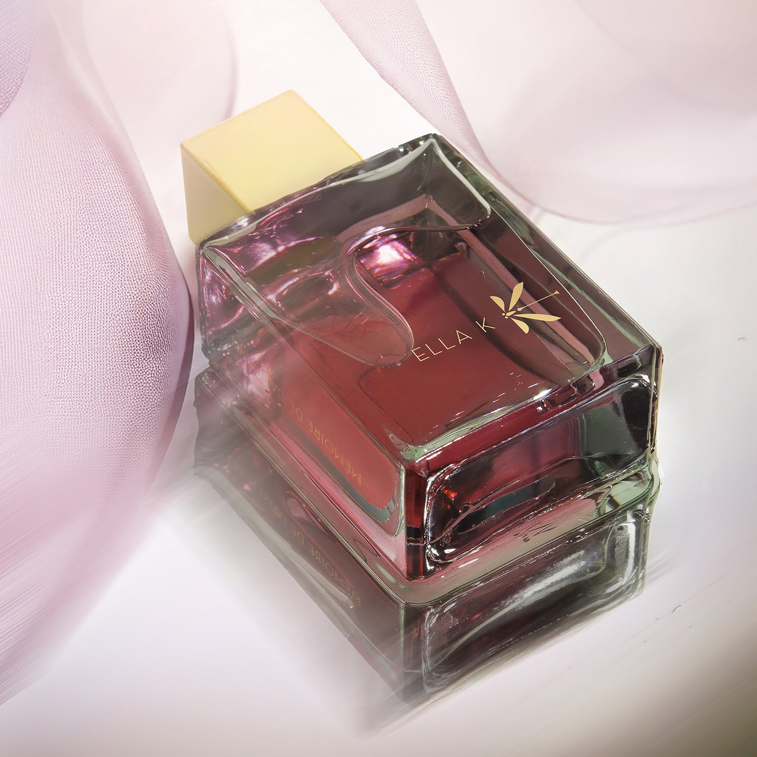 Le flacon du parfum « Mémoire de Daisen In » d’Ella K repose sur une surface réfléchissante, enveloppé d’un tissu rose délicat. Le bouchon doré et le liquide pourpre captent la lumière avec élégance – une composition raffinée entre parfum et esthétique.