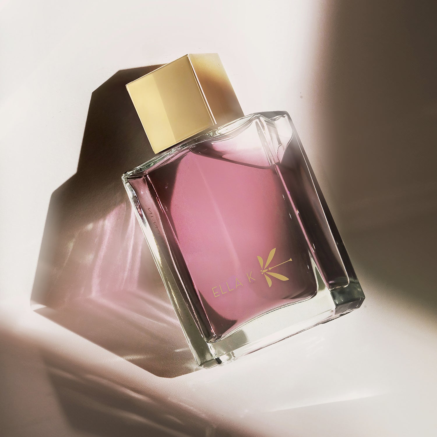 Le flacon du parfum « Mémoire de Daisen In » d’Ella K est posé verticalement sur une surface blanche, baigné de lumière chaude et d’ombres douces. Son design minimaliste, avec un bouchon doré et un liquide pourpre, souligne le caractère luxueux du parfum.