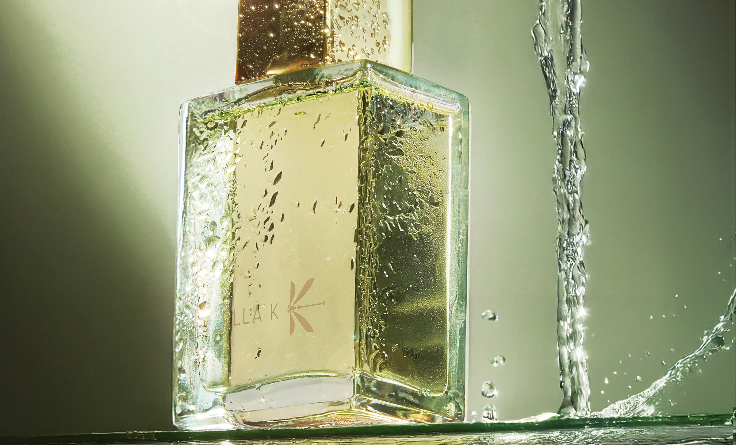 Flacon du parfum Pluie sur Ha Long d’Ella K avec bouchon doré, mis en scène avec des gouttelettes d’eau sur fond vert – inspiré par la baie mystique de Ha Long.