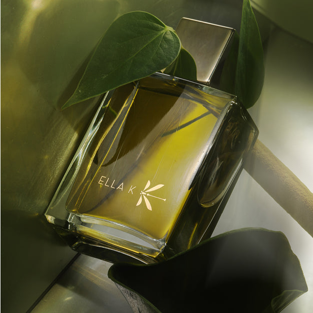 Flacon Poème de Sagano au parfum vert doré, entouré de feuilles – symbole d’élégance fraîche et de profondeur végétale